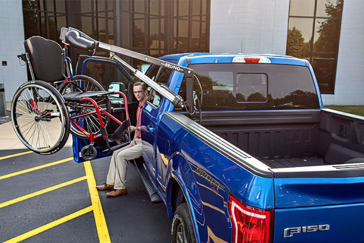 Blue pickup truck with a wheelchair lift; man exiting cab; wheelchair being loaded.