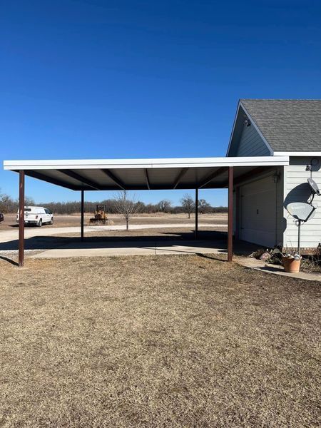 Carport attached to a house with metal roof, brown supports, and concrete floor.