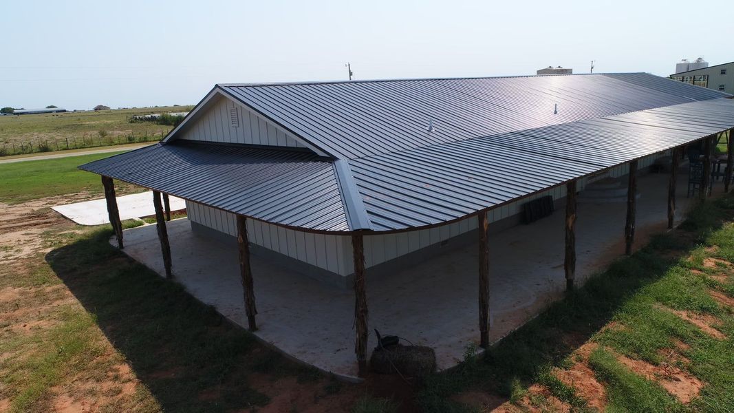 Building with a metal roof, porch, and white siding, set in a grassy field on a sunny day.