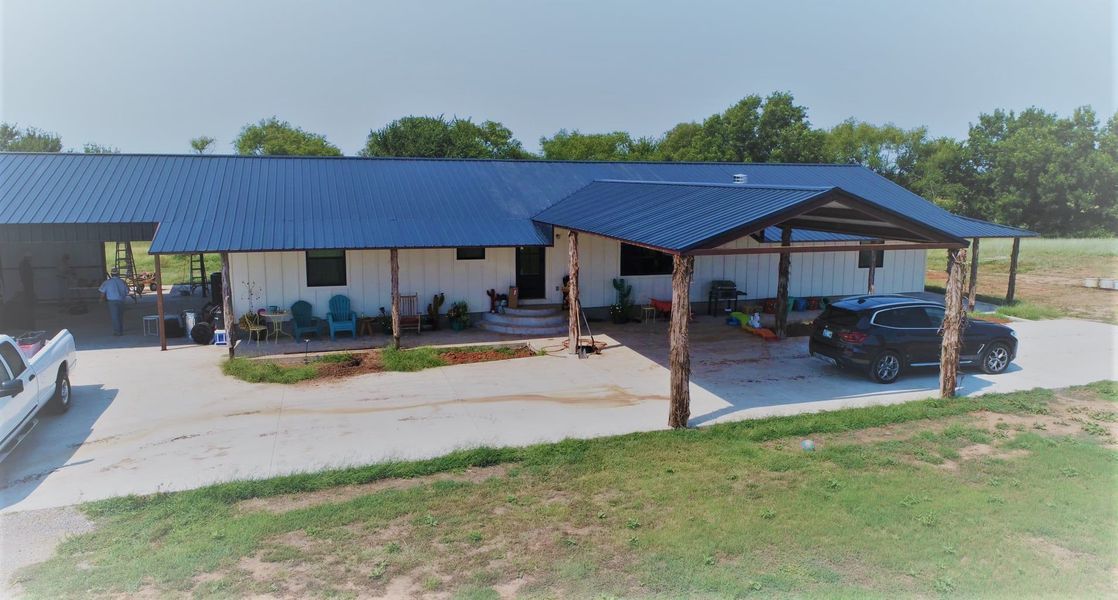 Blue-roofed, white-sided house with a carport; a car and truck parked in the driveway; green grass surrounding the property.