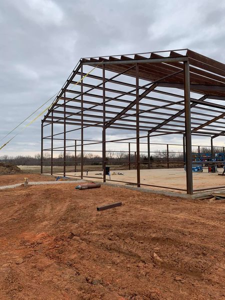 Steel frame of a building under construction on a dirt lot; cloudy sky overhead.