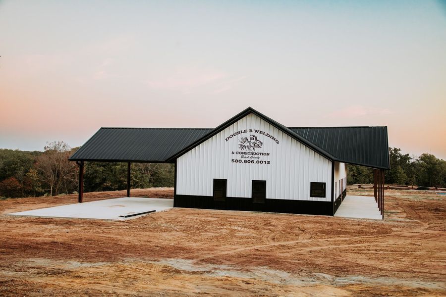 White barn with black roof and awning in a field. Signage on the barn.