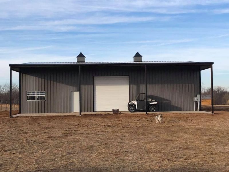 Gray metal building with a white garage door, small window, and extended overhang. Utility vehicle parked outside.