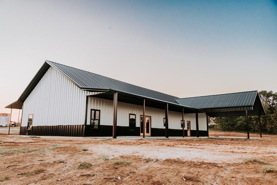 White and black metal building with a dark roof in a dry, open field.