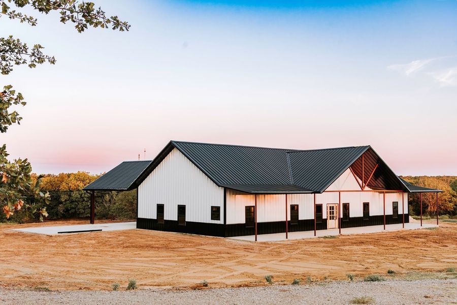 White and black barn with dark roof, located on a grassy field under a colorful sky.