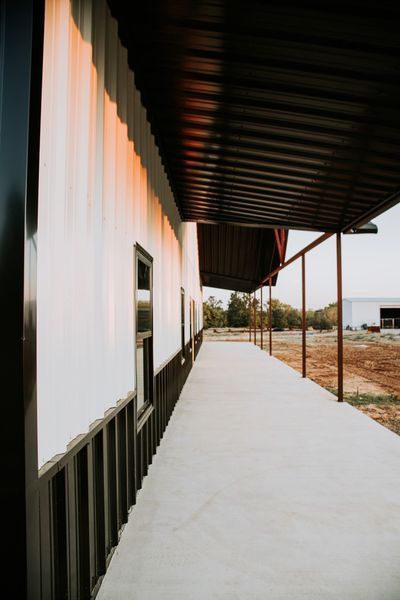 Exterior of a white building with a brown awning and walkway. A field is in the background.