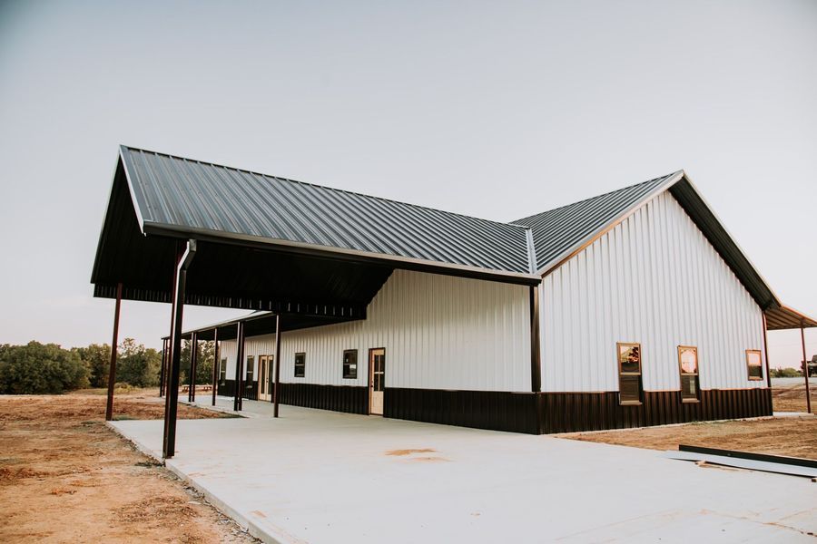 White and black barn-style building with a covered walkway and asphalt driveway against a clear sky.