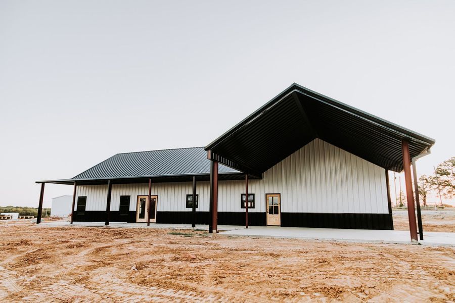 A long, modern building with a black and white exterior and a covered porch on a brown dirt field.