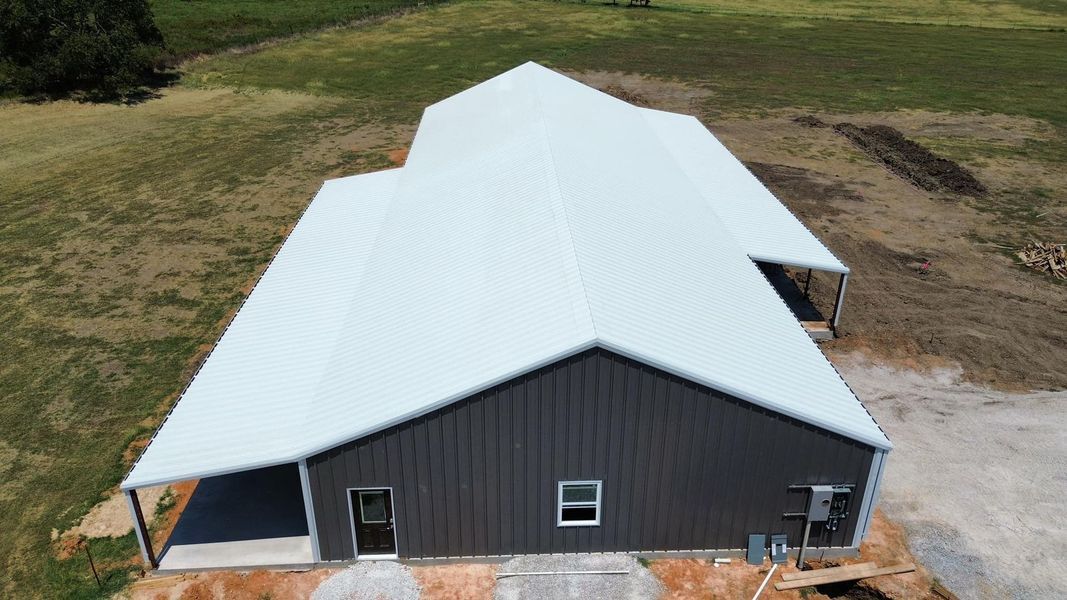 Dark gray metal-sided house with a large white roof, set in a grassy field.