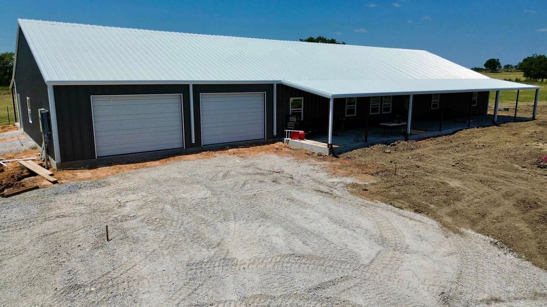 Gray building with white roof and garage doors, with a covered patio area and gravel driveway.