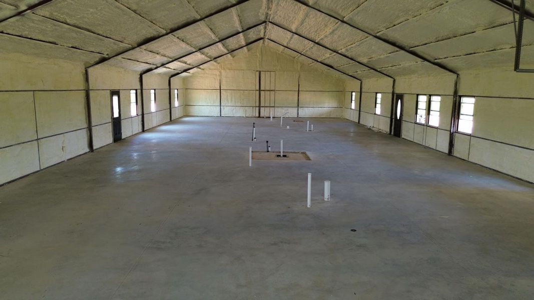 Large, empty building interior with concrete floor, white walls and ceiling, windows and black support beams.