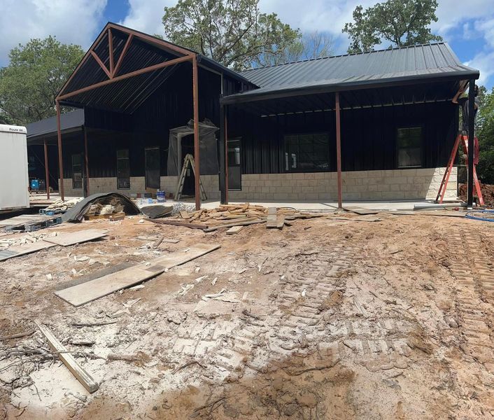 Building exterior under construction with metal roof and porch, surrounded by dirt and construction materials.
