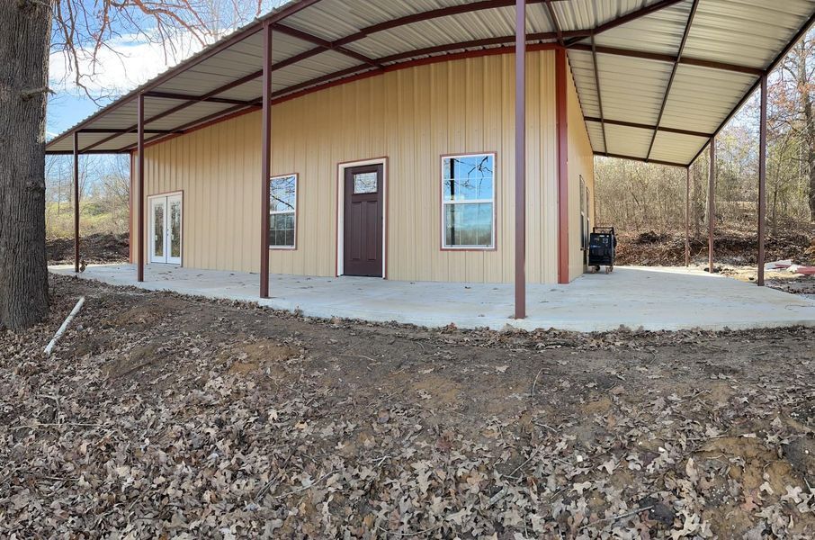Tan metal building with brown trim and large covered porch on concrete slab.