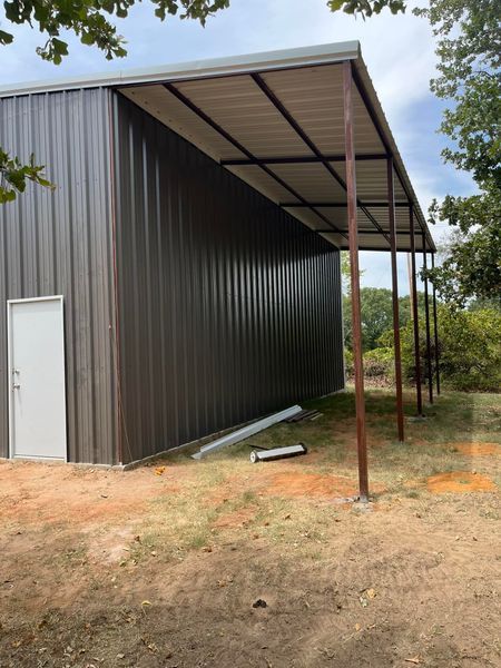 Brown metal building with attached covered awning, set on dirt and grass.