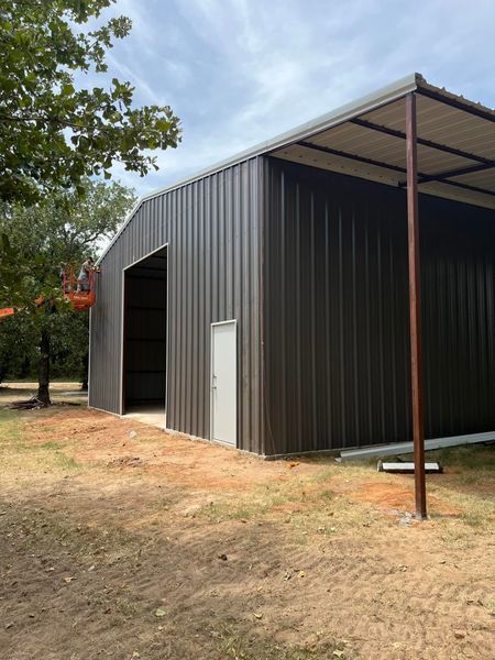 Brown metal barn with open entrance, small door, and awning on a cloudy day.