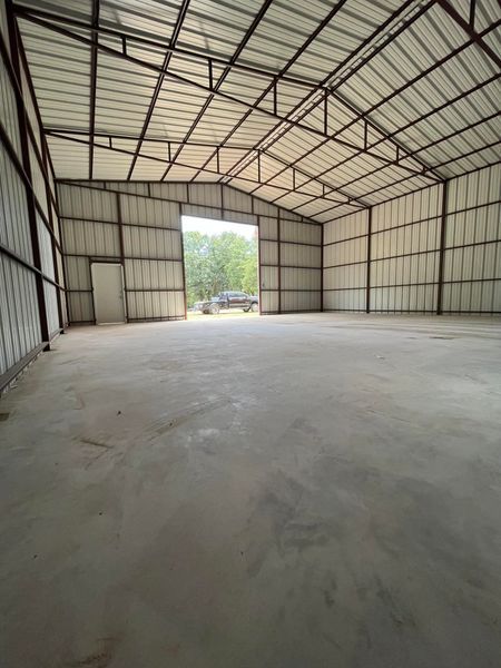 Large, empty metal warehouse interior with open doorway, cement floor, and steel frame.