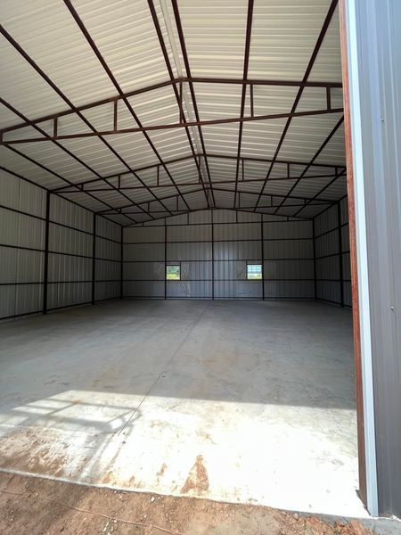 Interior of an empty metal building with concrete floor and natural light from two windows.