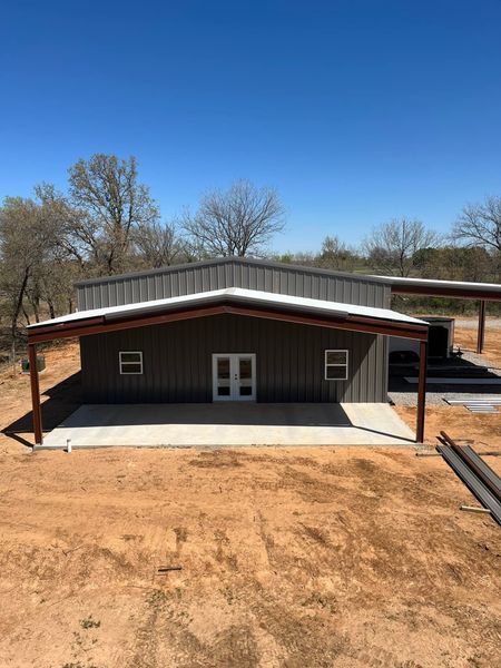 Metal building with a brown exterior, white doors, and a concrete patio on a sunny day.