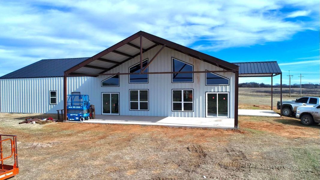 Metal-sided house with a large open front porch.  Blue sky background.  A blue lift and truck are present.