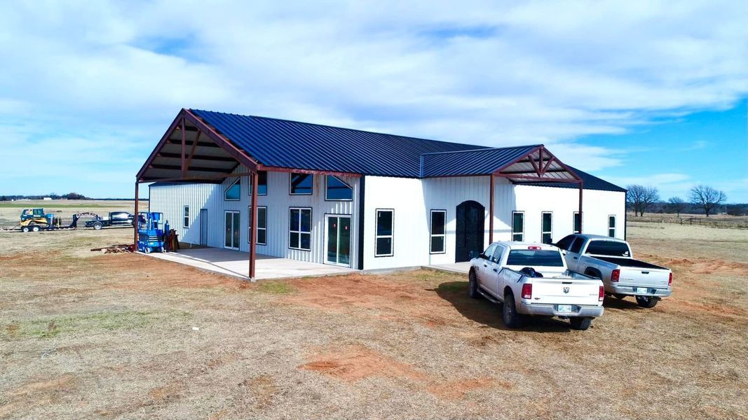White metal barn home with a covered porch, two parked trucks, and a blue sky.