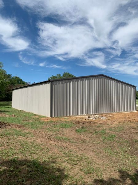 Large gray metal building with a dark roof against a partly cloudy blue sky.