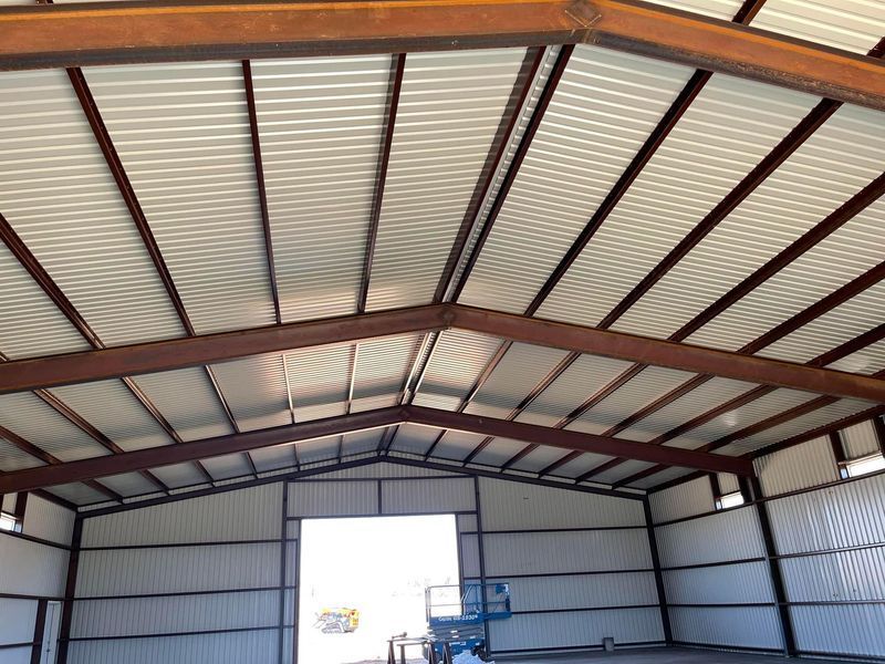 Interior view of a metal building with a white corrugated roof and brown steel beams.