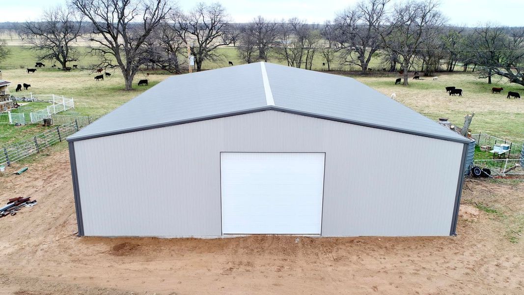 Metal building with a large white door, surrounded by a grassy field with grazing cattle.