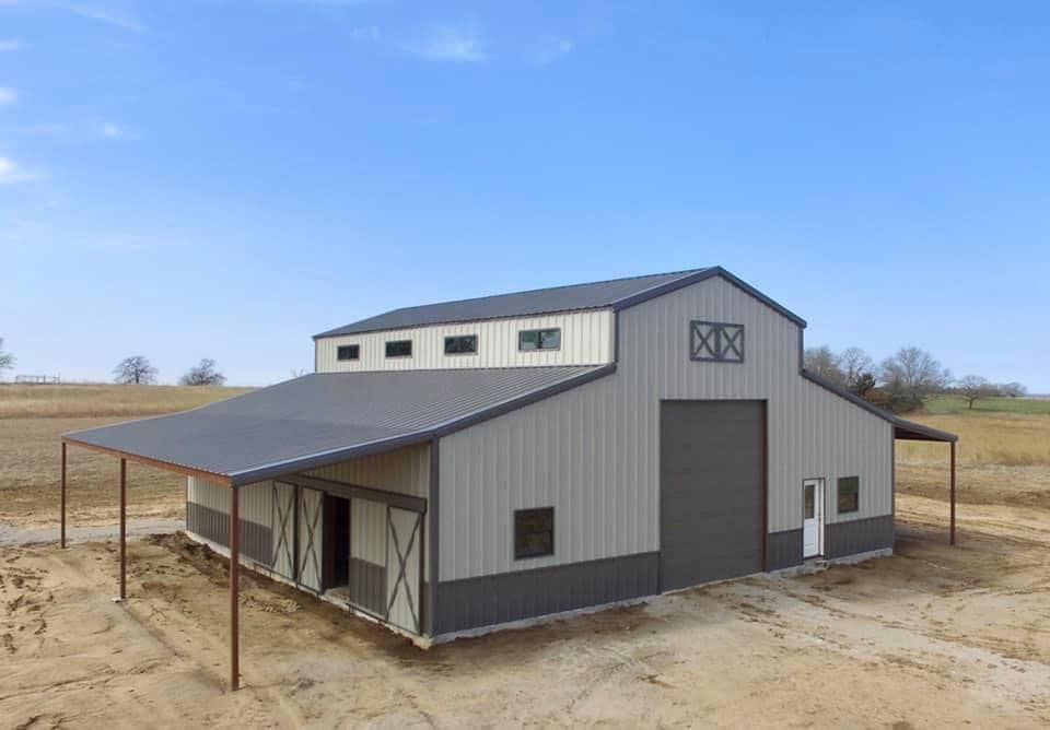 Large metal barn with gray and white siding, covered entryway, and a blue sky.