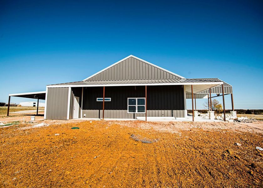 Gray metal building under construction, brown dirt, blue sky, covered porch.