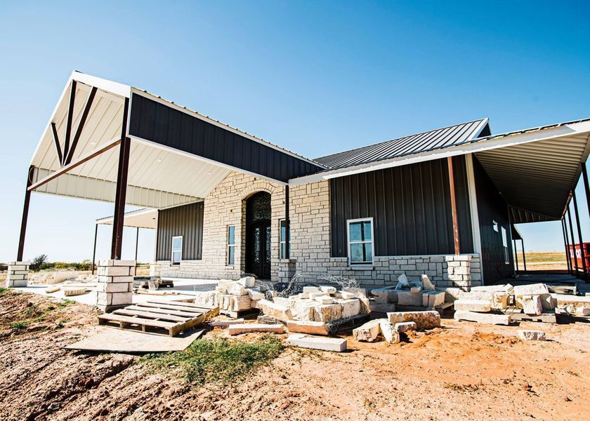 Building under construction: stone and dark metal siding, porch with exposed beams, blue sky.