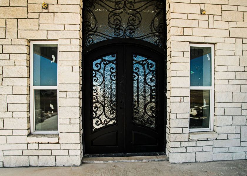 Black ornate double doors with arched top, flanked by two narrow windows, on a stone building.