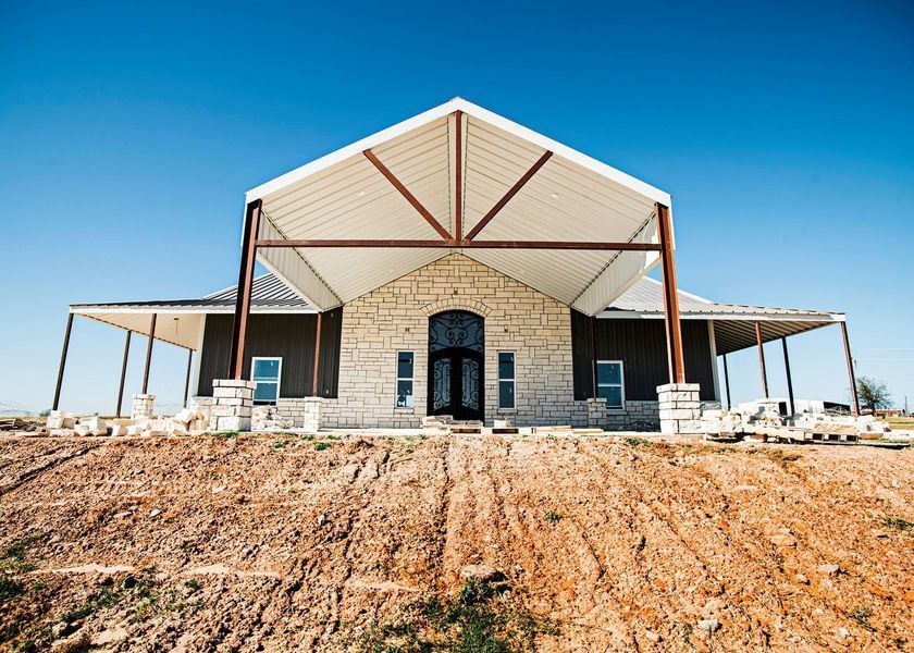 Modern home with a stone facade, brown siding, and a large metal roof under a blue sky.