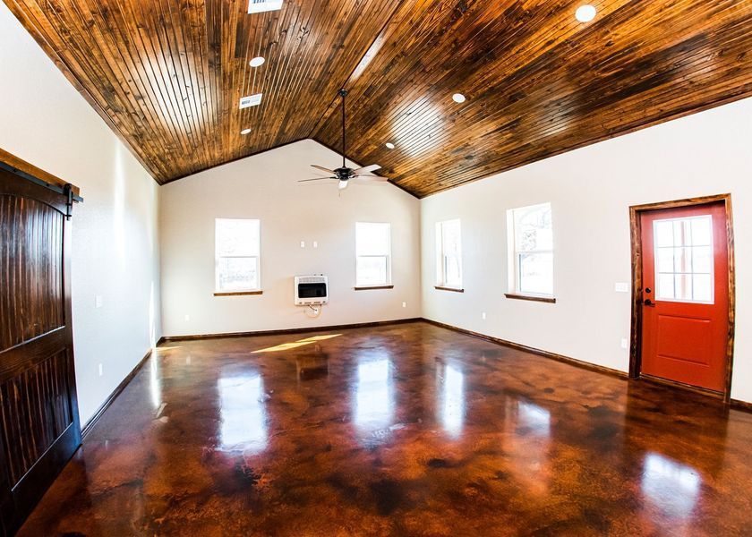 Empty room with wood ceiling, stained concrete floor, white walls, windows, and red door.