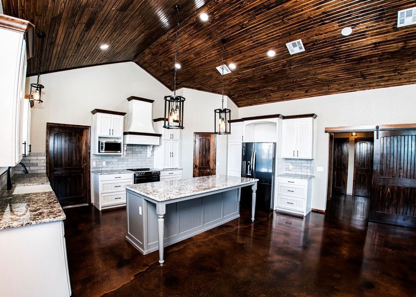Kitchen with stained wooden ceiling, white cabinets, gray island, and brown floor.