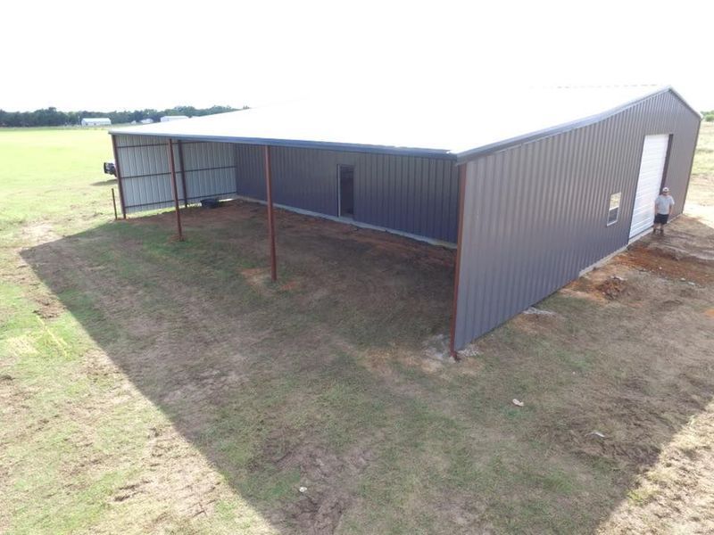 Gray metal barn with a covered side on a grassy field; person near the door.