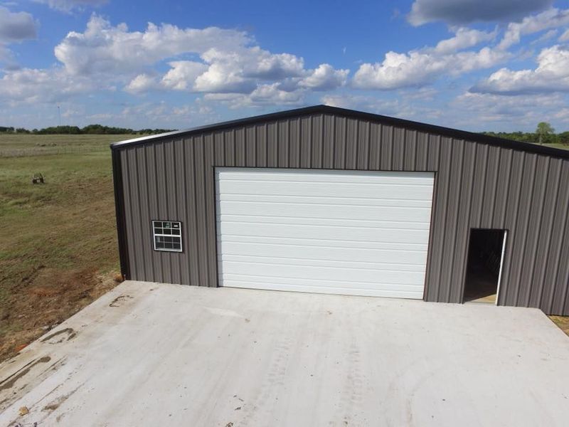 Gray metal building with a large white garage door and concrete slab.
