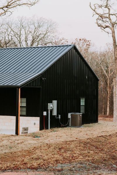 Black metal-sided building with dark blue roof; windows and electrical components on the exterior; set in a brown field with bare trees.
