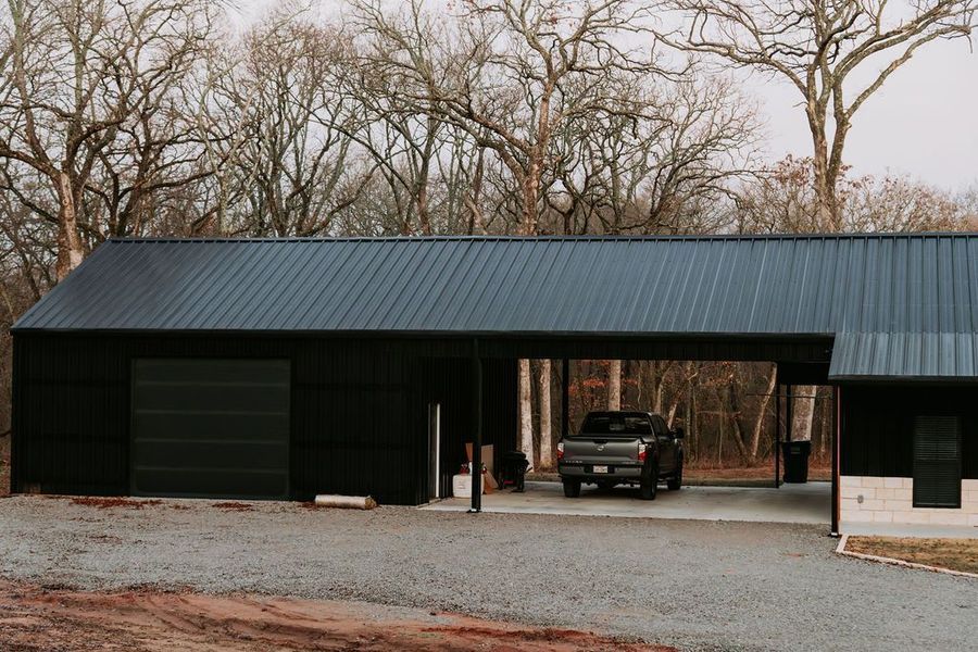 Black building with a covered drive-through, a truck parked inside. Exterior shot with trees in background.