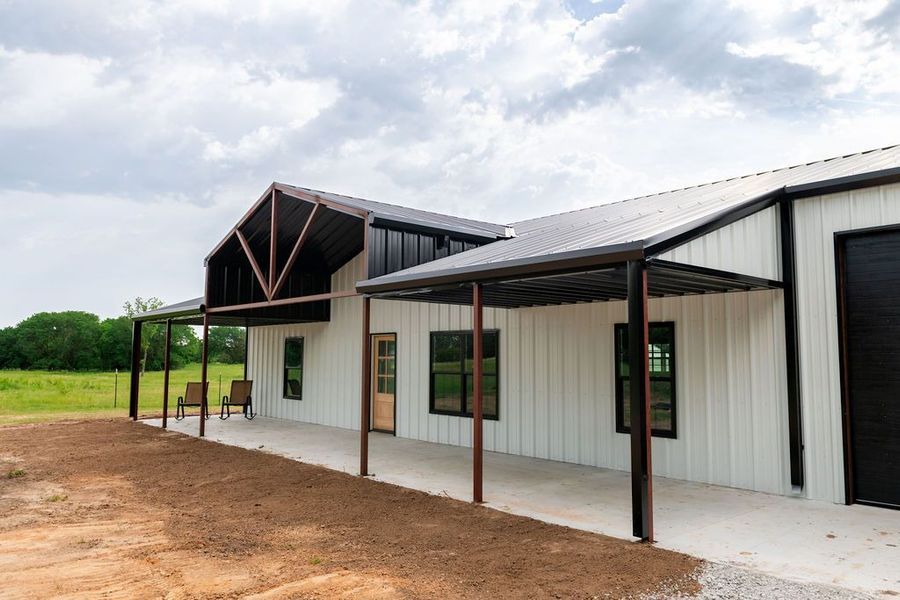 White modern barn-style building with a covered porch and brown accents under a cloudy sky.