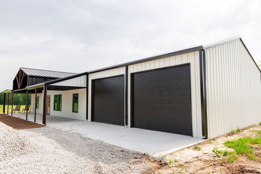 White and black metal building with two garage doors and a porch, set on a concrete pad.