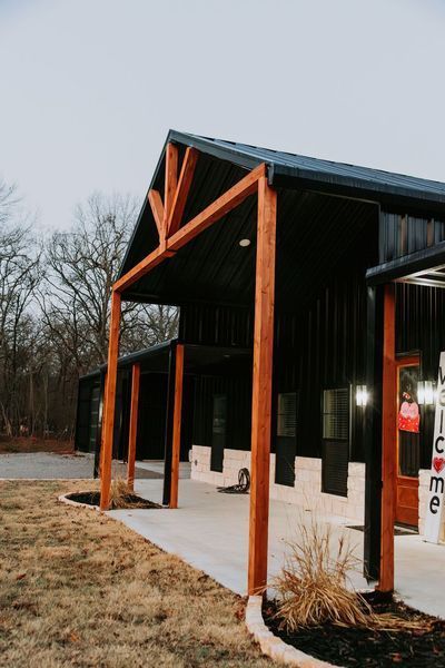 Black metal-sided building with brown wooden supports and a concrete walkway.