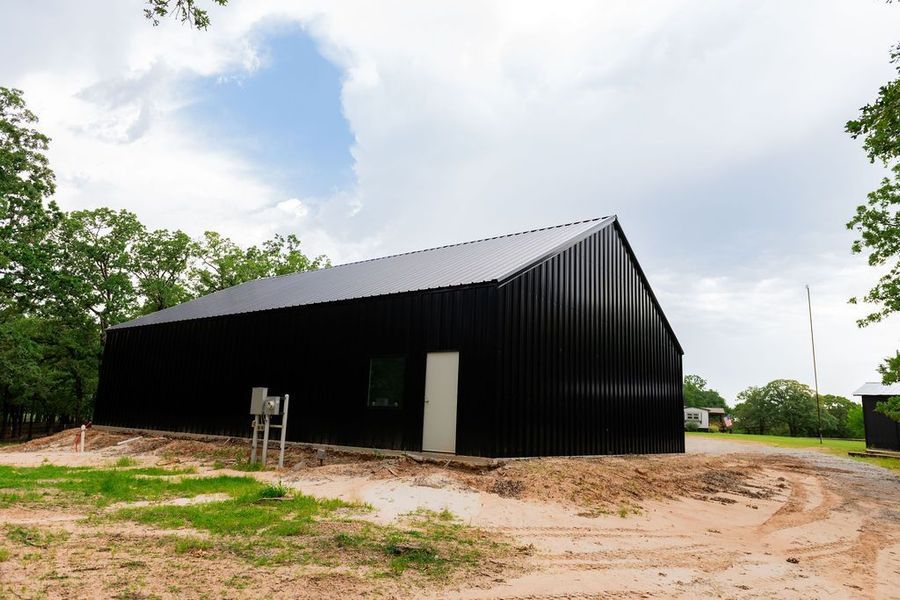 Black metal-sided building with angled roof. White door, small window, and utility box on the side.