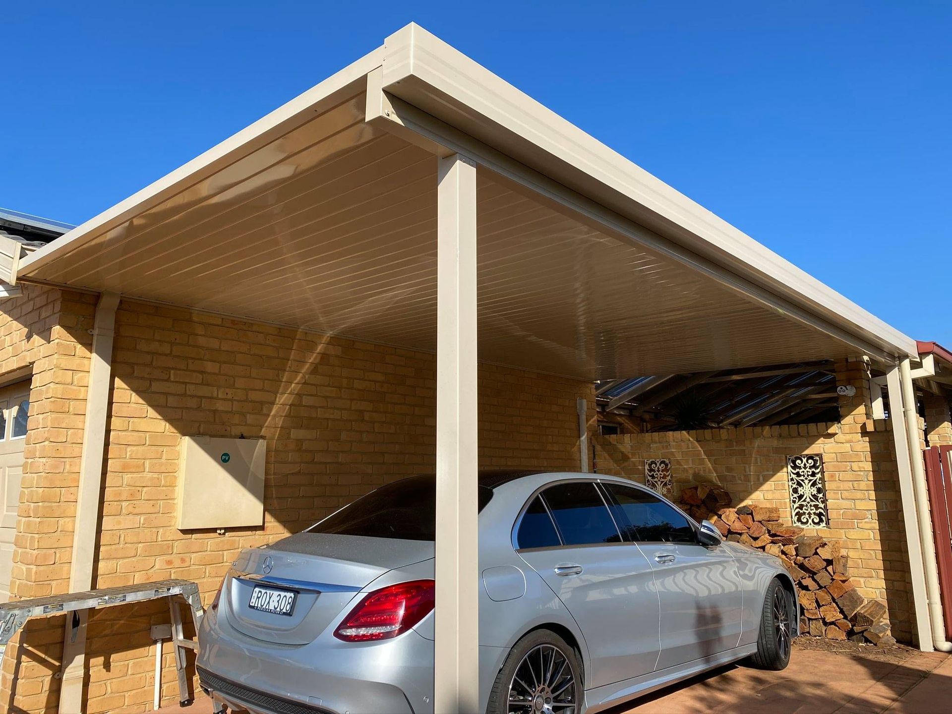 A white patio cover is being installed on the side of a brick house.