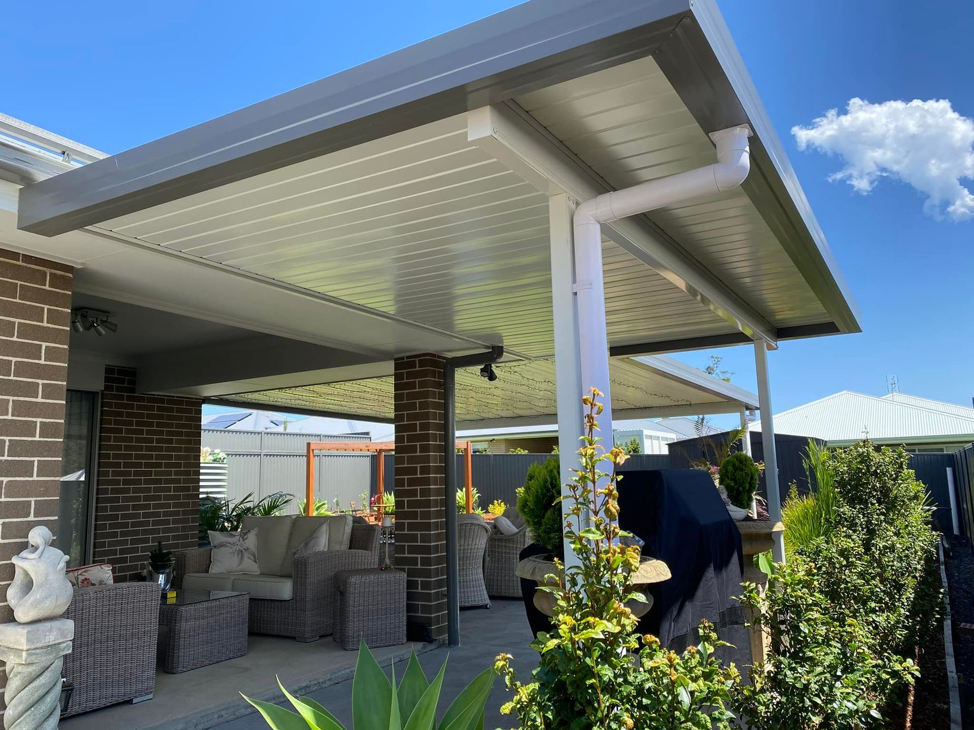 A white patio cover is being installed on the side of a brick house.