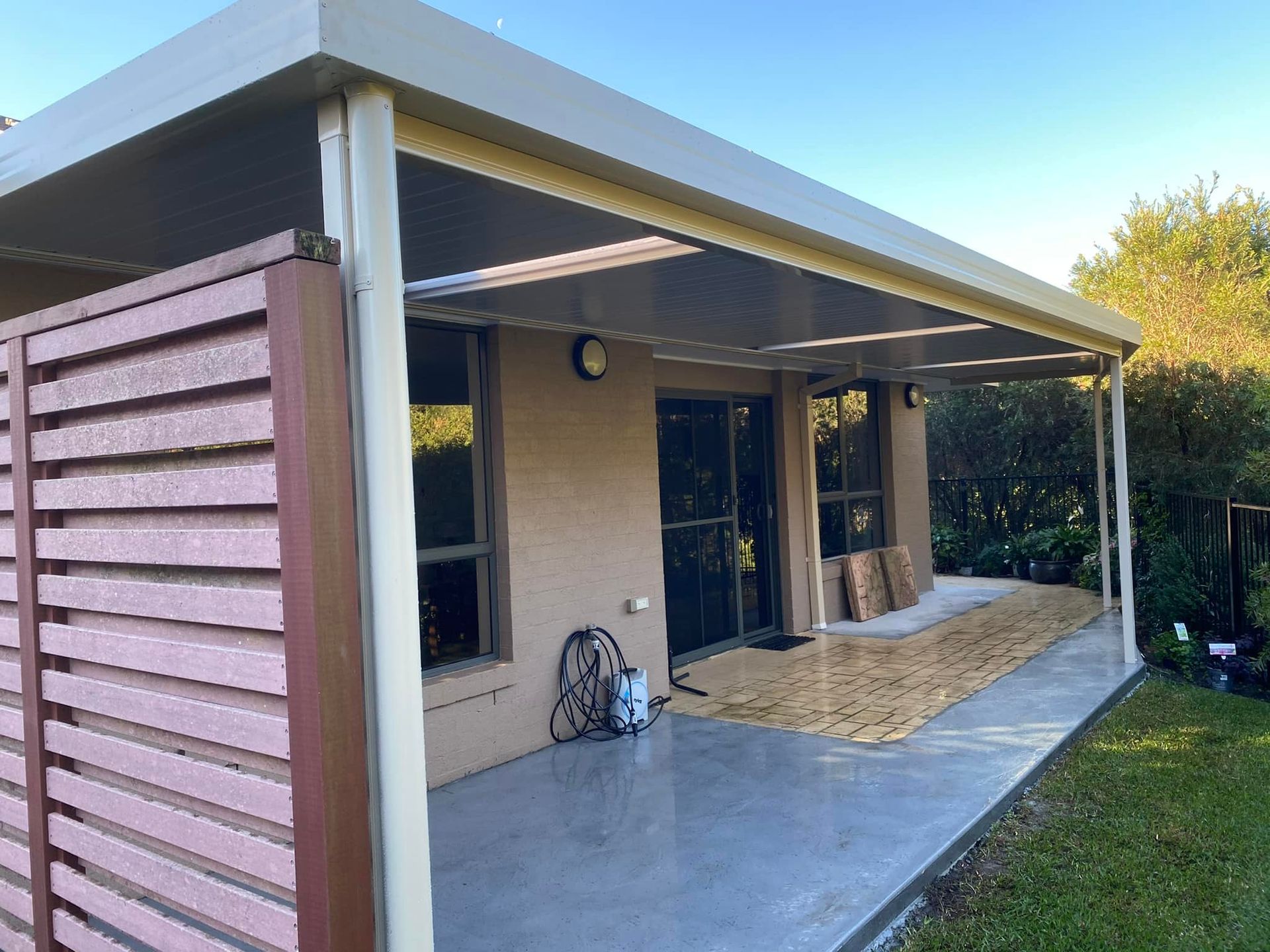A white patio cover is being installed on the side of a brick house.