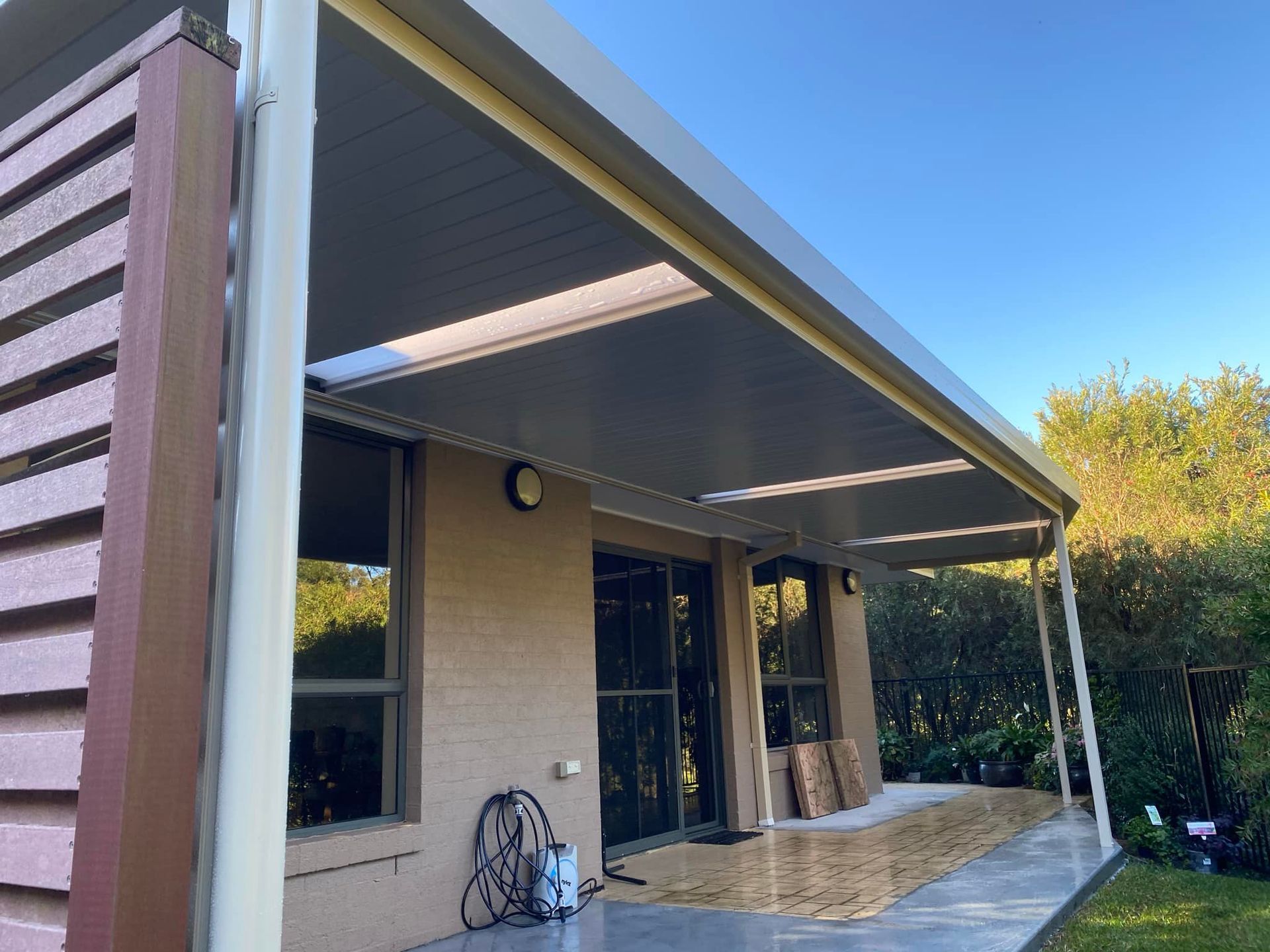 A white patio cover is being installed on the side of a brick house.
