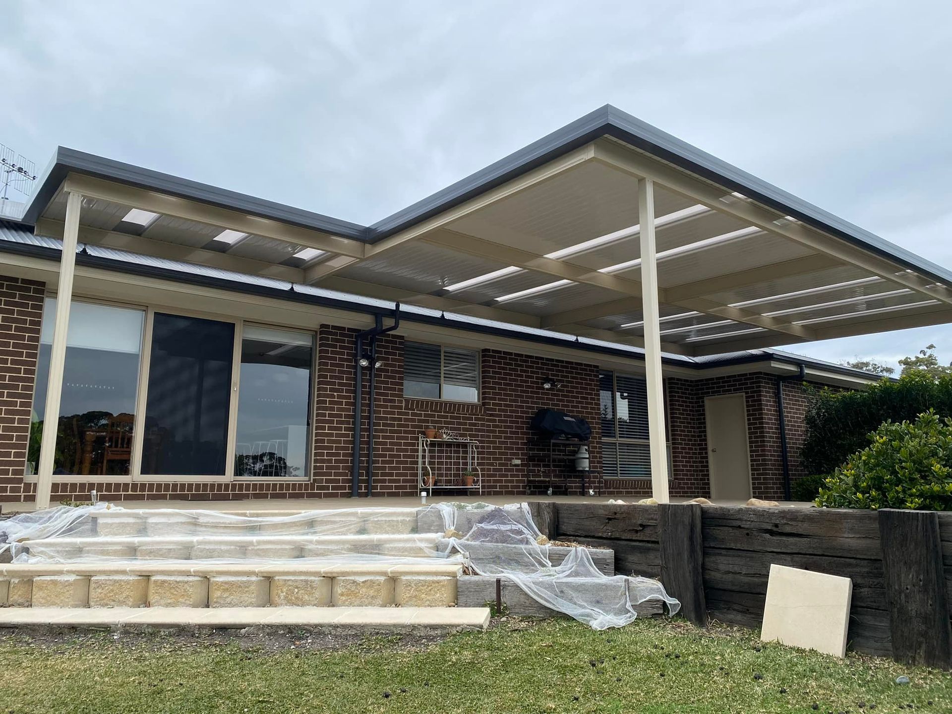 A white patio cover is being installed on the side of a brick house.