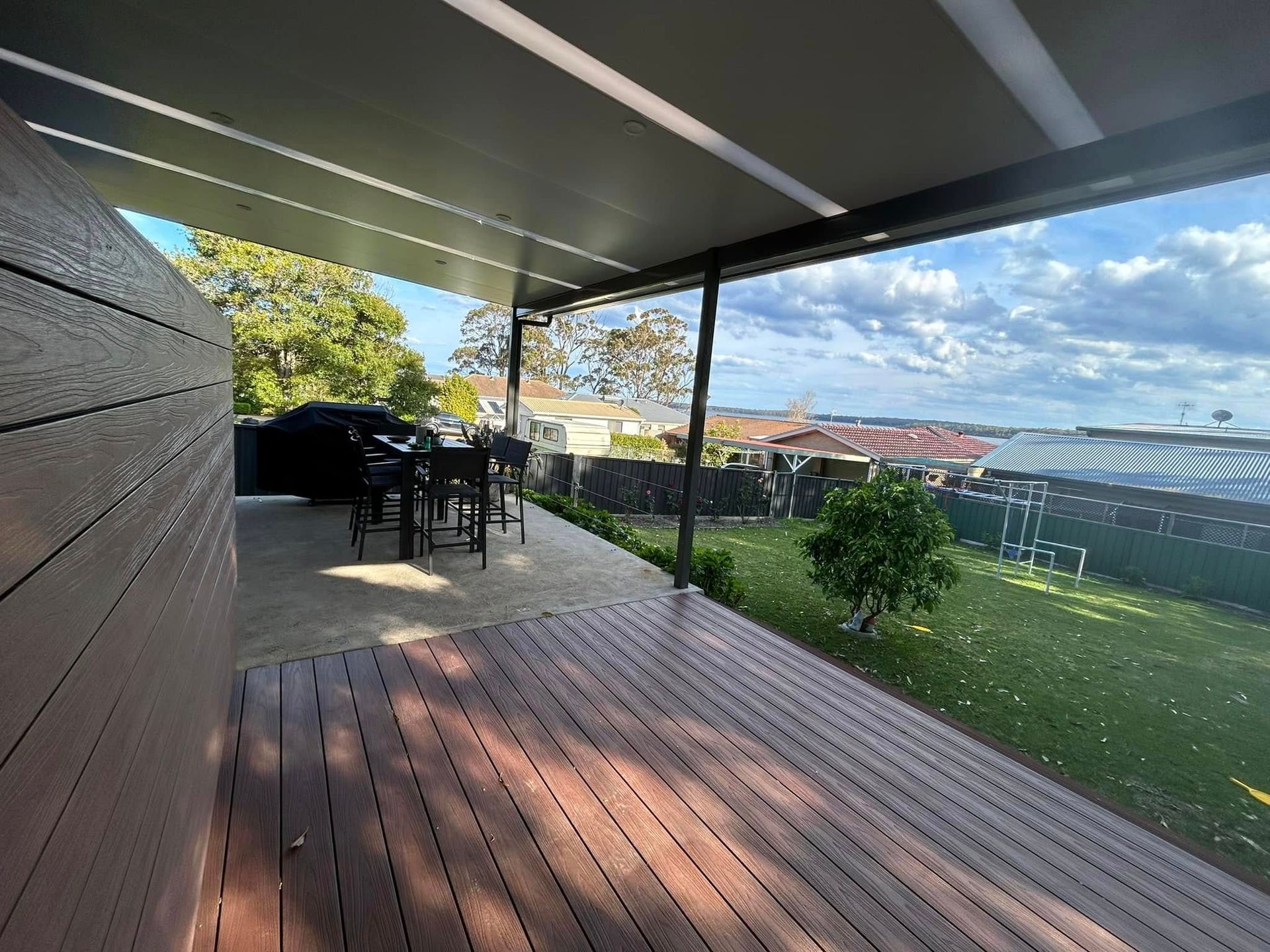 A wooden deck with a table and chairs under a canopy.