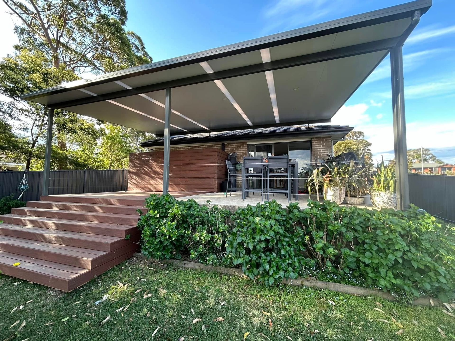 A white patio cover is being installed on the side of a brick house.