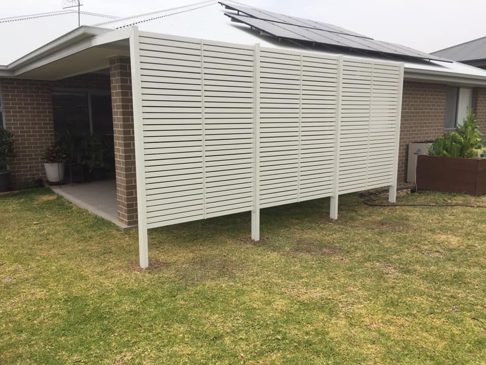 A white patio cover is being installed on the side of a brick house.